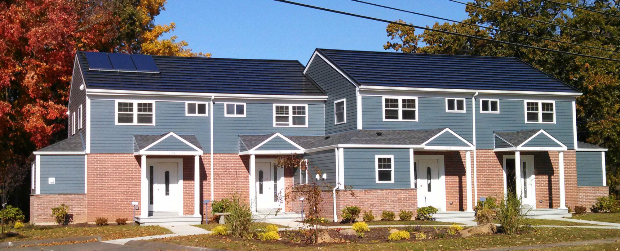 Townhouse apartments with both brick and blue clapboard siding. A solar panel on one roof. A landscaped area in front.